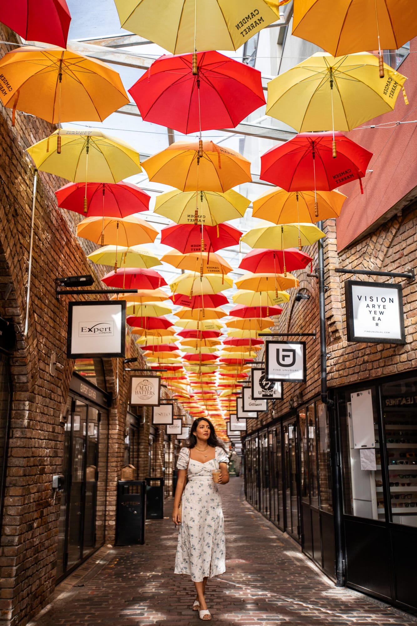 Anoushka in a white sun dress walking under a canopy of colourful umbrellas in Camden Market