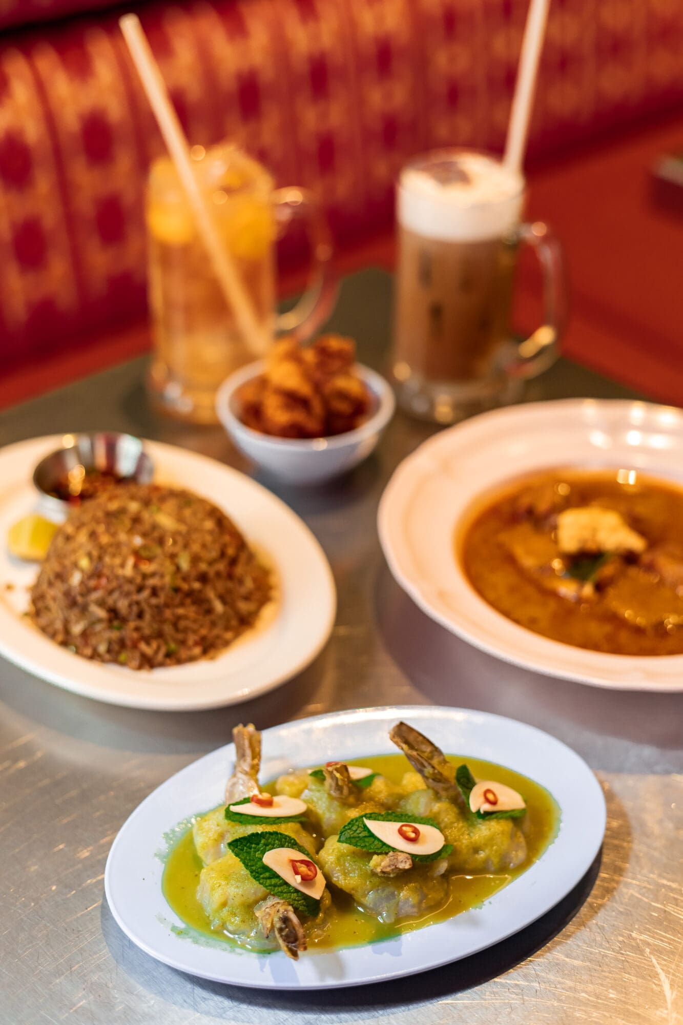 A close up shot of dishes at Thai Restaurant Speedboat Bar in Chinatown London. In the foreground is the prawn ceviche, with several juicy prawns in a green spicy sauce.