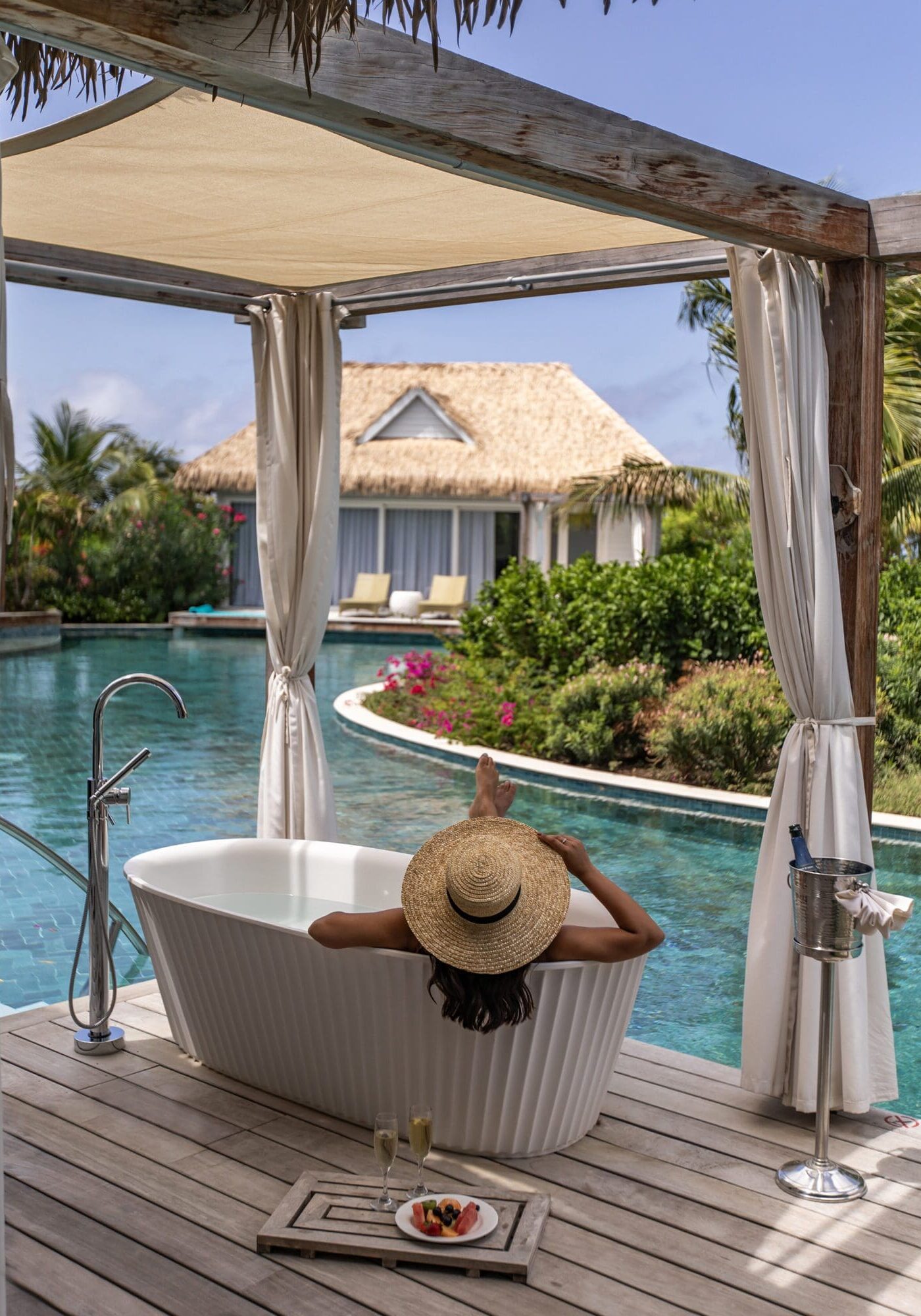 The back of a girl's head wearing a hat, sitting in a tub overlooking a pool in a villa at Sandals Royal Curacao